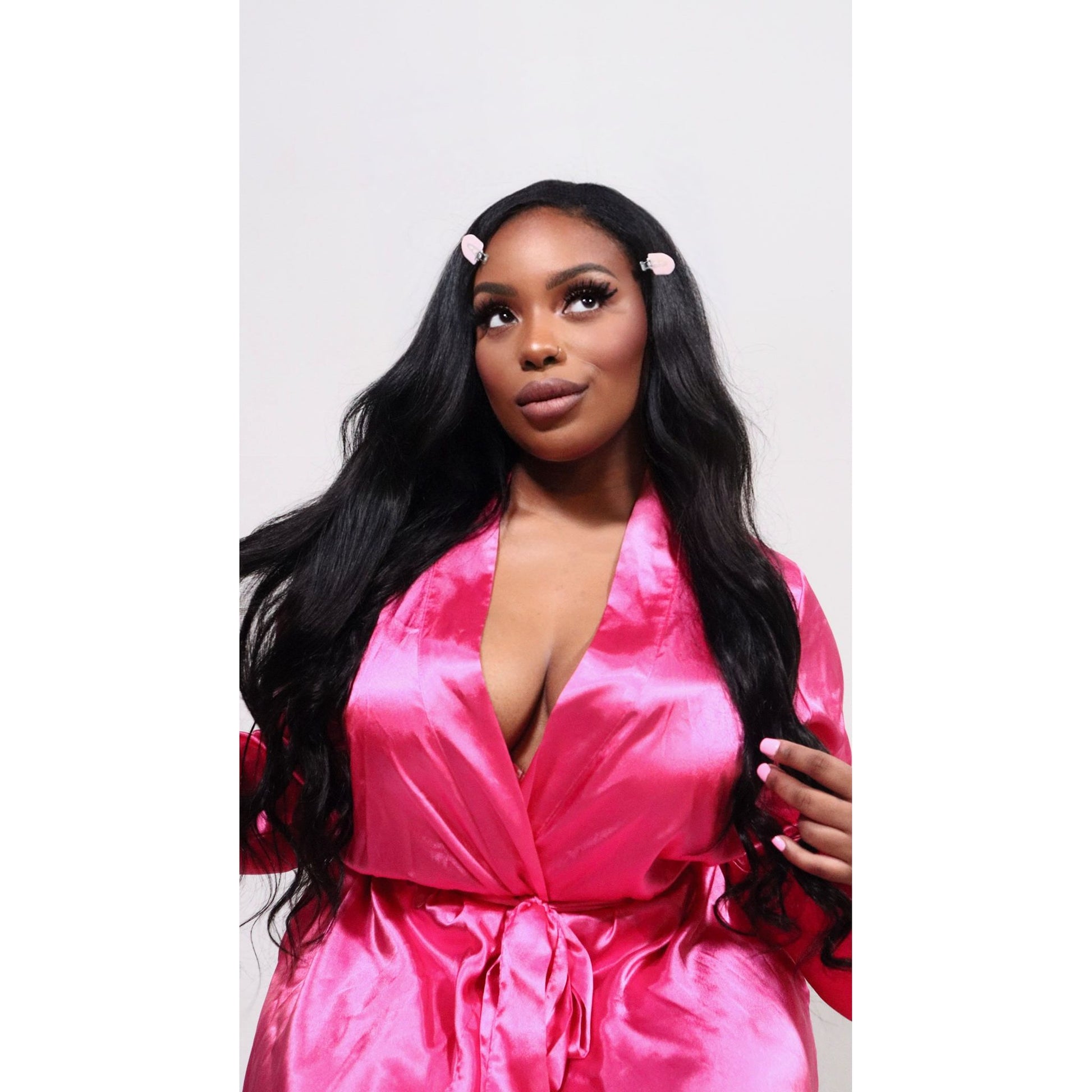 Woman wearing a pink satin robe against a white background modeling hair extensions Bodywave 