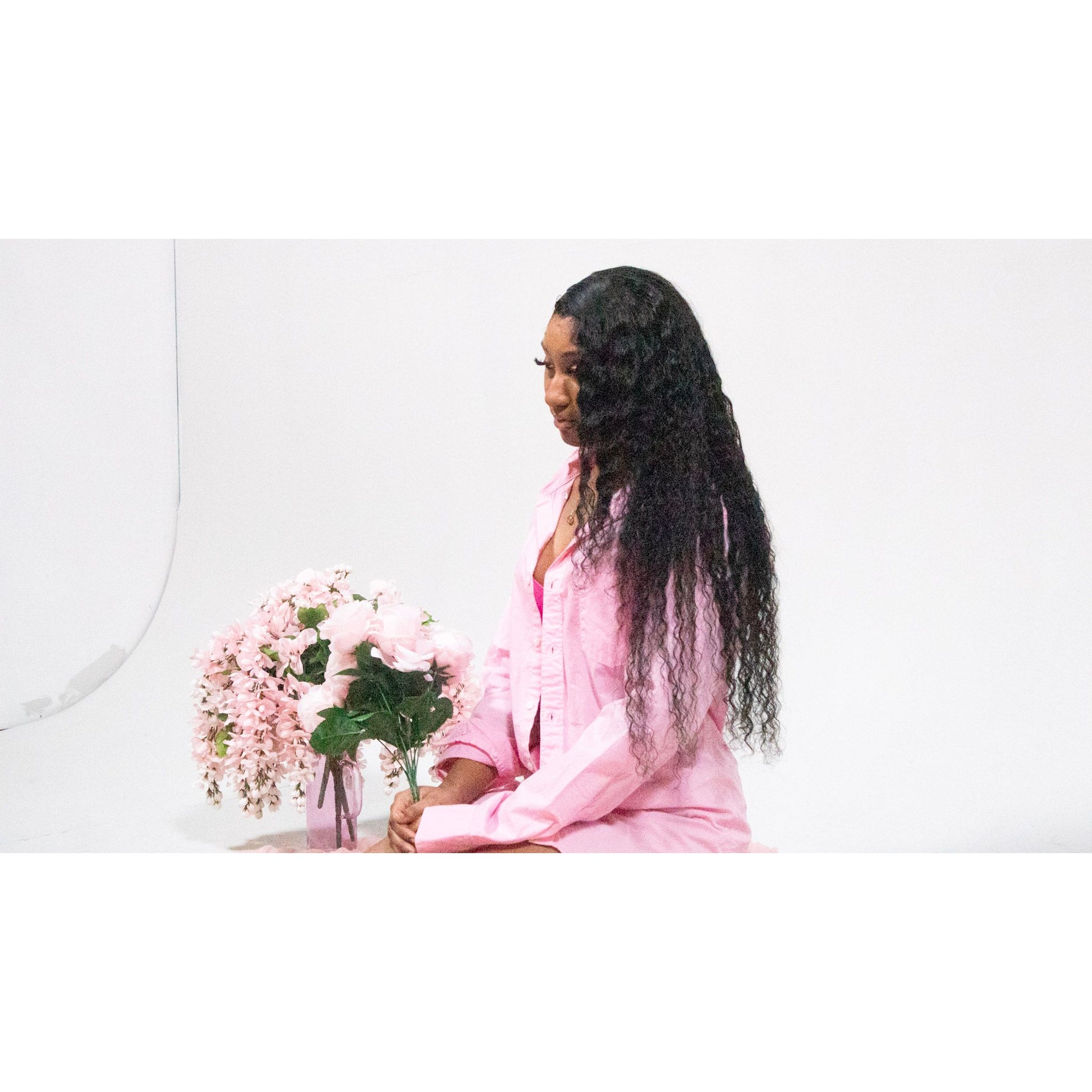 Woman in pink pajamas sitting with a vase of flowers on a white background showcasing Deepwave hair 
