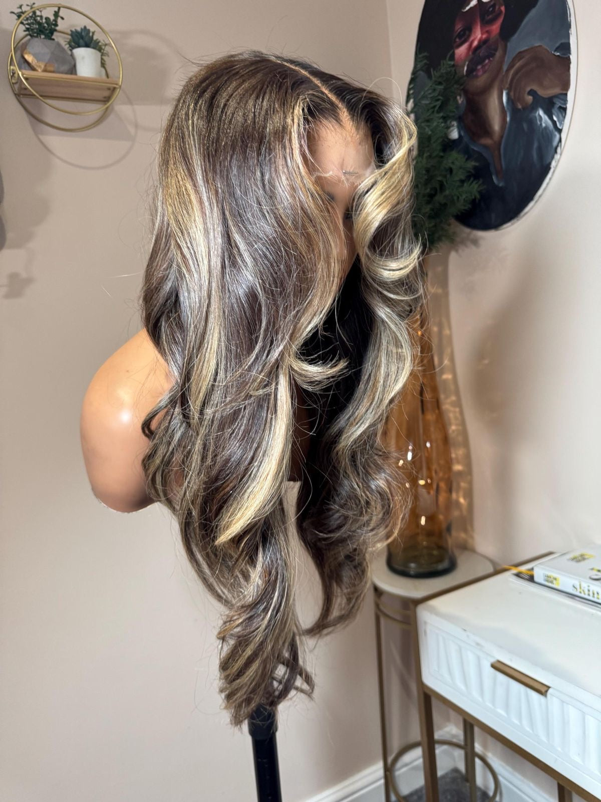 Mannequin head with long, wavy blonde highlights hair styled in a room setting.