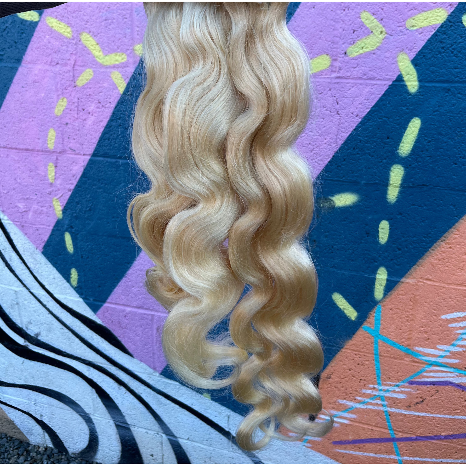 Blonde bundles Bodywave  hair extensions held by a hand against a colorful abstract background