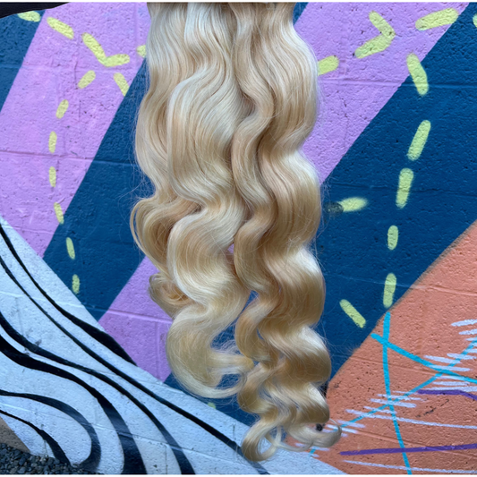 Blonde bundles Bodywave  hair extensions held by a hand against a colorful abstract background
